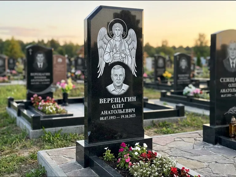 Памятник с гравировкой иконы: стела с резным навершием и нимбом в золоте — гравировка образа Спасителя, высокие разросшиеся туи полукругом, работа «Мельникова» в Туле