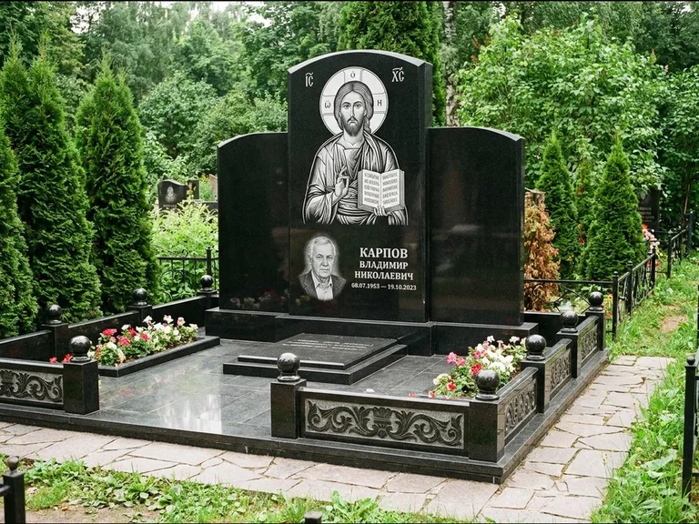 Памятник с гравировкой иконы: широкая панорамная стела с золочёным нимбом — гравировка образа Матроны Московской, цветник с белыми хризантемами, работа «Мельникова» в Туле