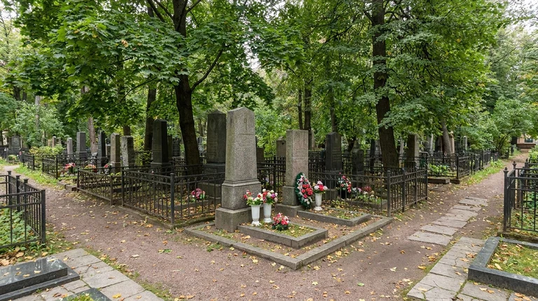 Гранитный памятник на участке кладбища Памяти жертв 9-го января в Санкт-Петербурге среди старых деревьев